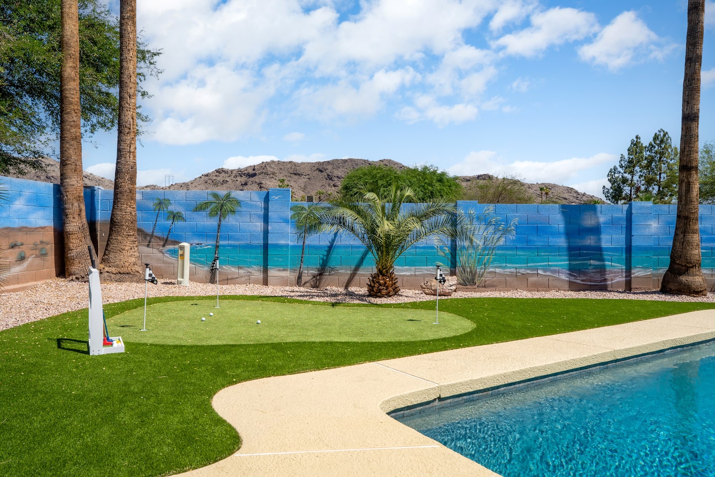 Putting green beside the pool at South Mountain Vista, backed by palm-and-beach murals with the South Mountain ridge behind