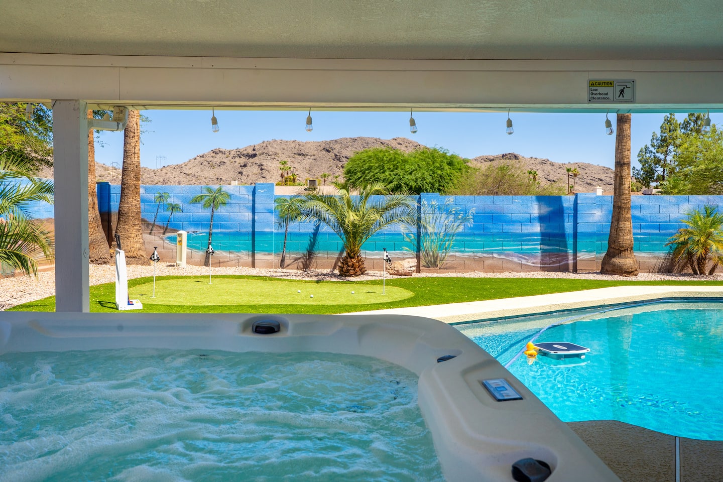 Bubbling hot tub under the covered patio at South Mountain Vista, looking across the pool and putting green to the mountains