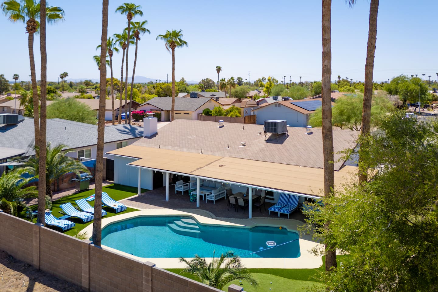 Aerial view of South Mountain Vista: the pool, striped loungers on the turf, the covered patio and the putting green among tall palms