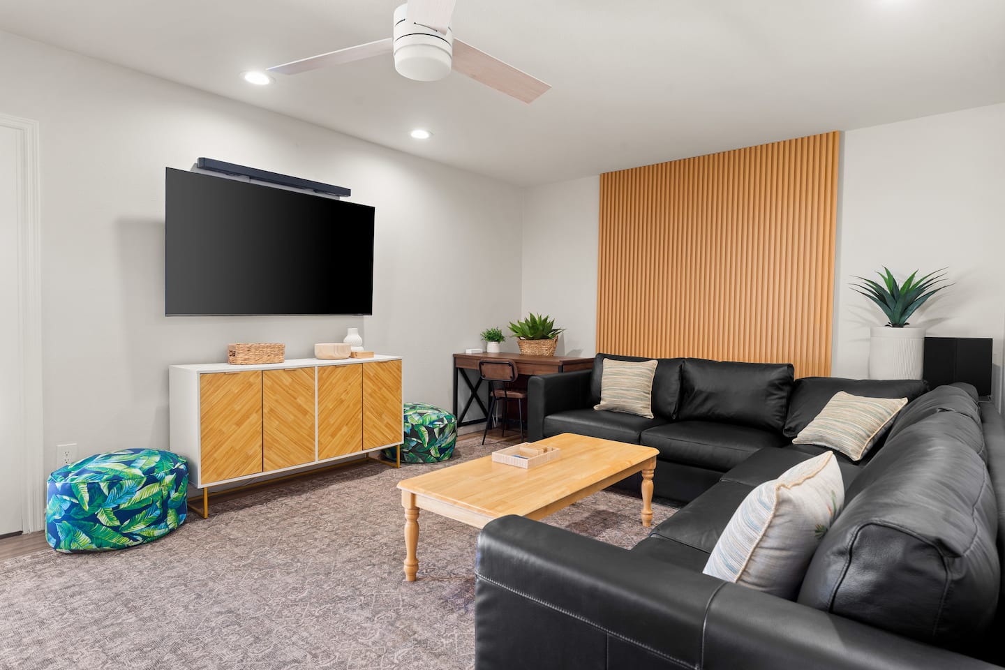 Living room at South Mountain Vista with a black leather sectional, a slatted wood accent wall, a large TV and a desk