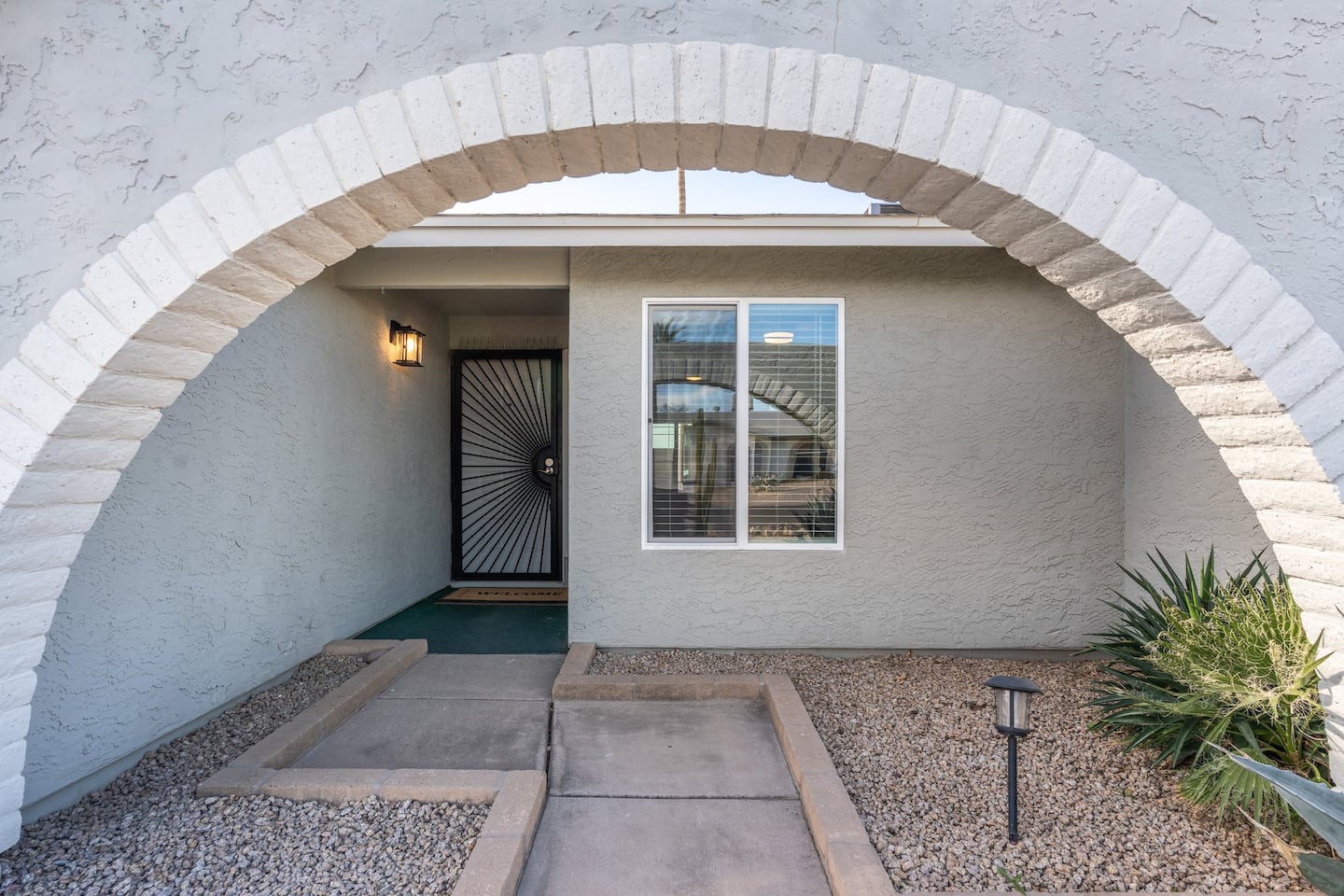 The arched front entry at South Mountain Lagoon, with a white brick arch, a security screen door and desert plantings