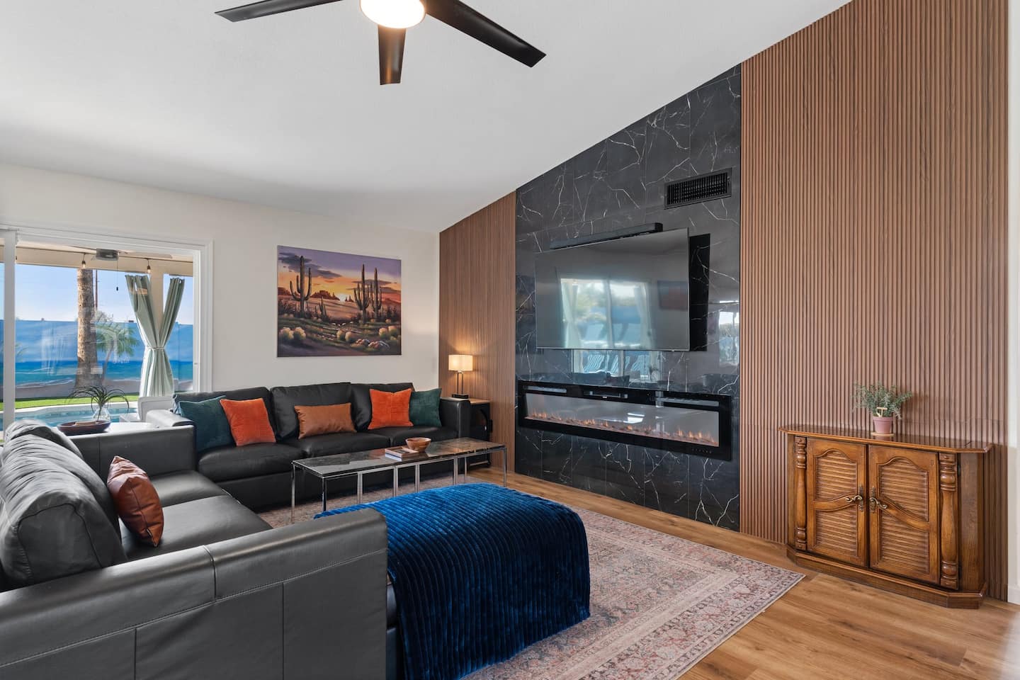 Living room at South Mountain Lagoon: a black leather sectional, a slatted wood accent wall with a marble fireplace and TV, and the pool through the sliding door