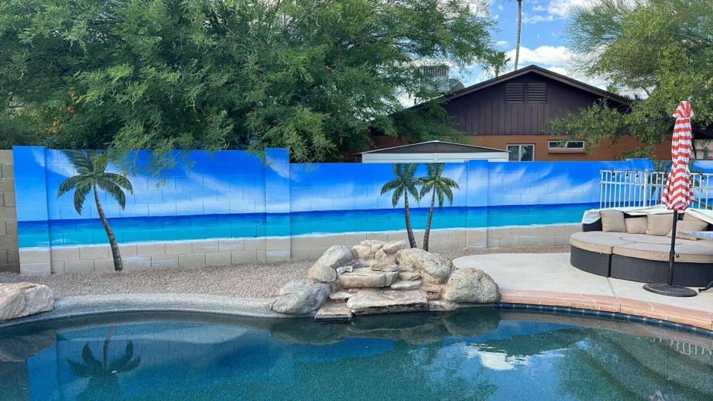 The newest mural at South Mountain Oasis: a painted beach with palms along the block wall, above the rock waterfall at the pool's edge